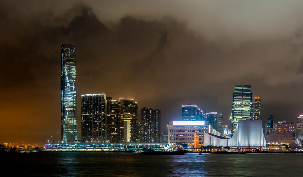 Hong Kong skyline lit up at night across Victoria Harbour, with the ICC tower on the Kowloon side