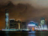 Hong Kong skyline lit up at night across Victoria Harbour, with the ICC tower on the Kowloon side