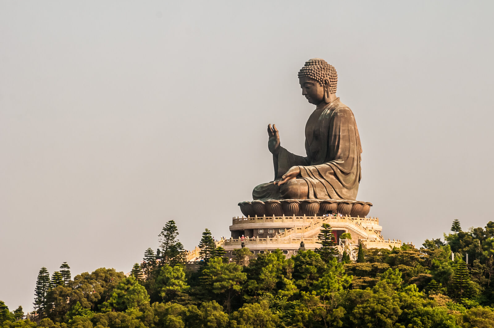 The bronze Tian Tan Big Buddha seated on a hilltop above green forest on Lantau Island, Hong Kong