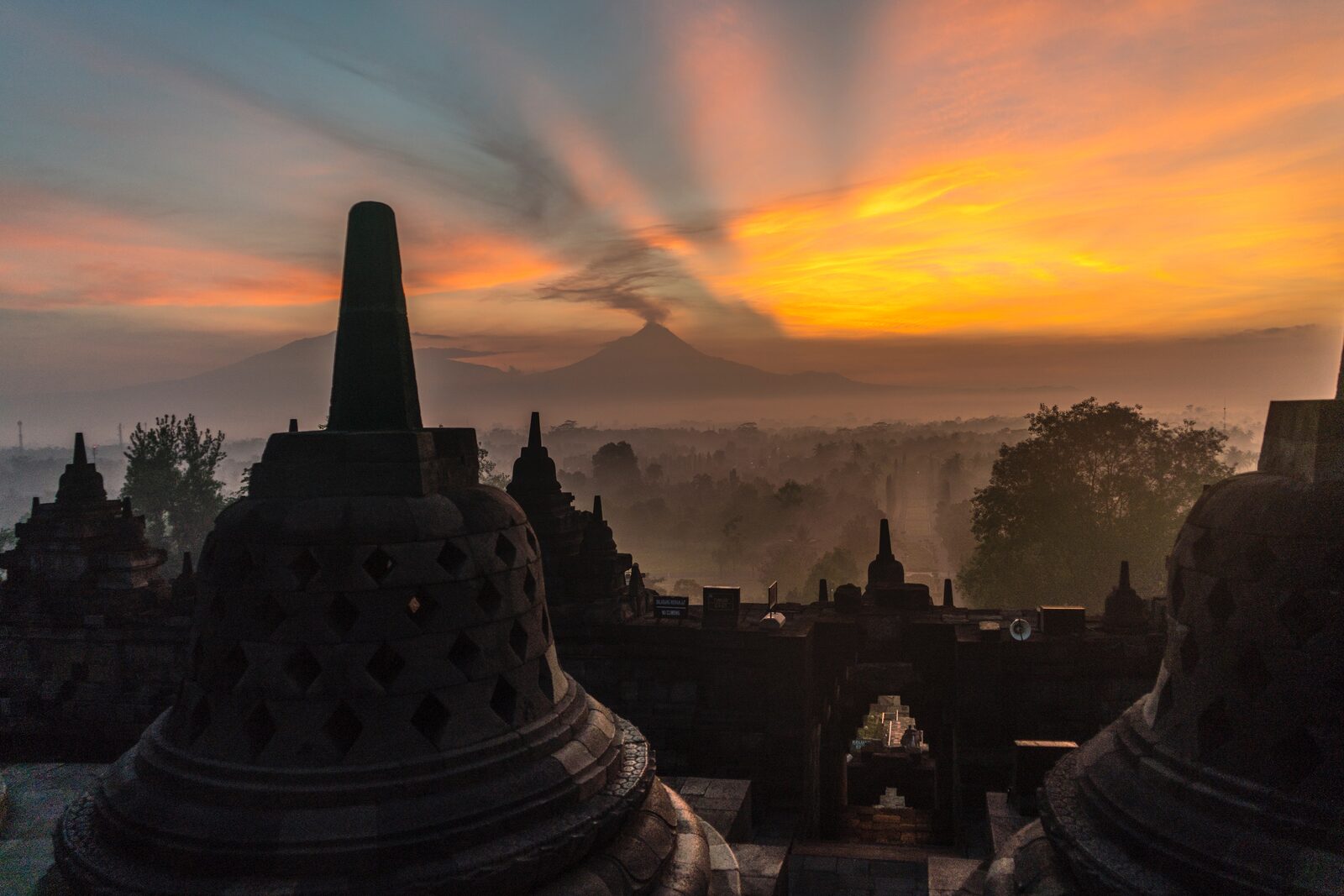 Borobudur temple stupas at sunrise with a volcano behind, Java, Indonesia