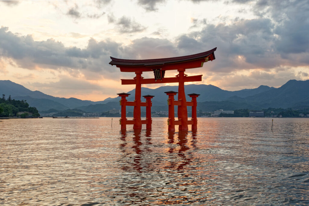 The vermilion Itsukushima floating torii gate standing in the sea at sunset off Miyajima island near Hiroshima, Japan