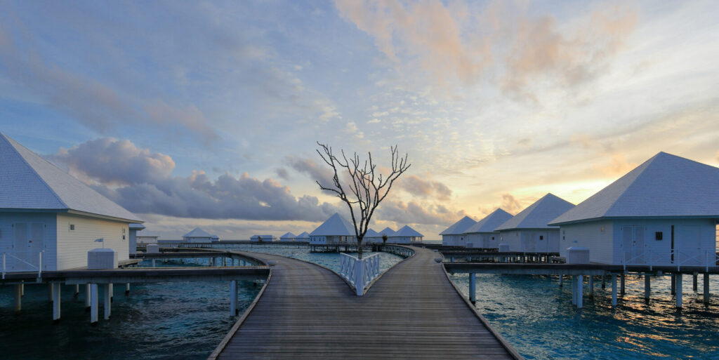 Overwater villas and a wooden boardwalk at sunset in the Maldives