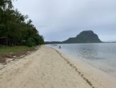 View across a calm Mauritius lagoon to Le Morne Brabant mountain from a quiet sandy beach