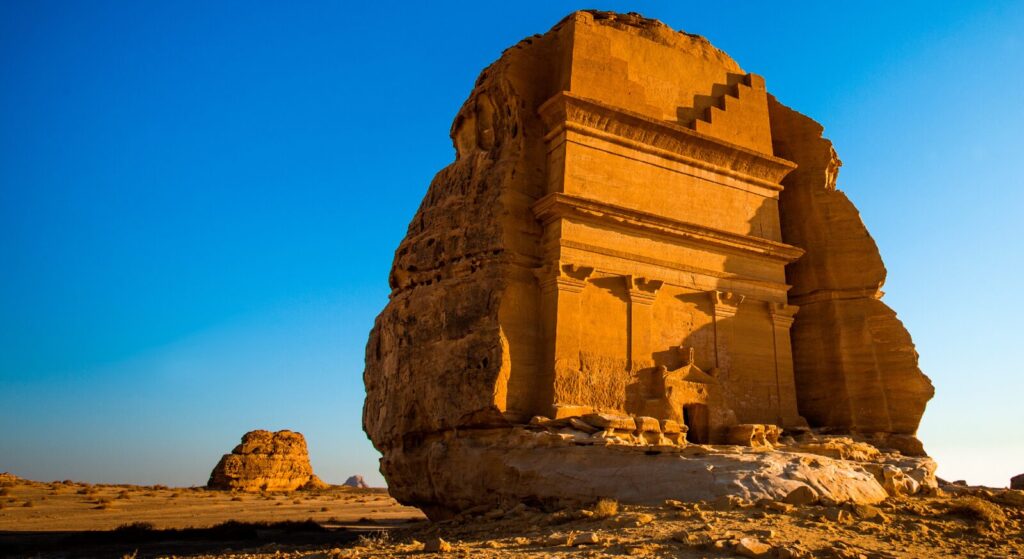 Qasr al-Farid rock-cut tomb at Hegra, AlUla, Saudi Arabia, glowing at sunset under a clear blue sky