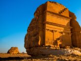 Qasr al-Farid rock-cut tomb at Hegra, AlUla, Saudi Arabia, glowing at sunset under a clear blue sky