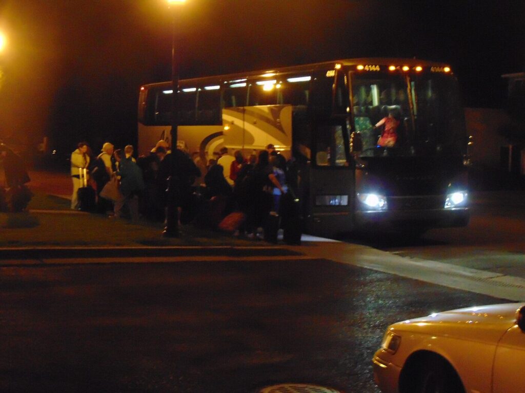 Travellers with luggage boarding a shared seat-in-coach tour bus at a pickup point