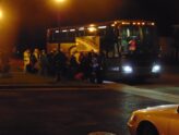 Travellers with luggage boarding a shared seat-in-coach tour bus at a pickup point