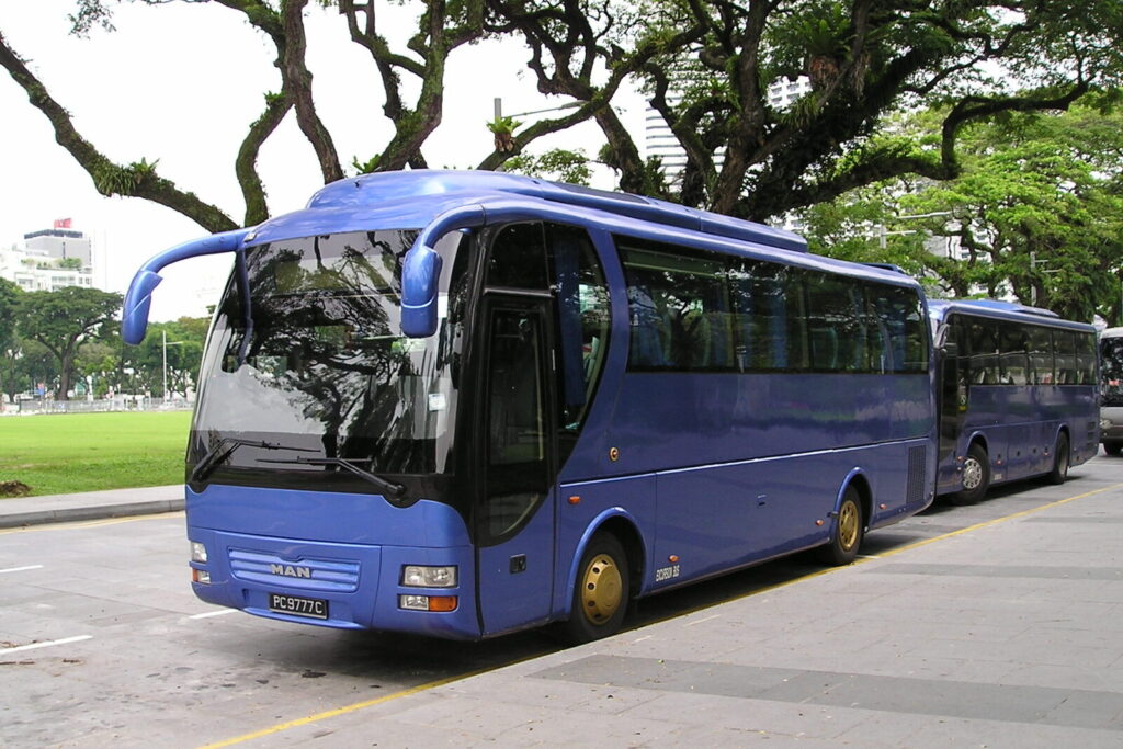 A blue tour coach parked under trees in Singapore, ready for a group transfer