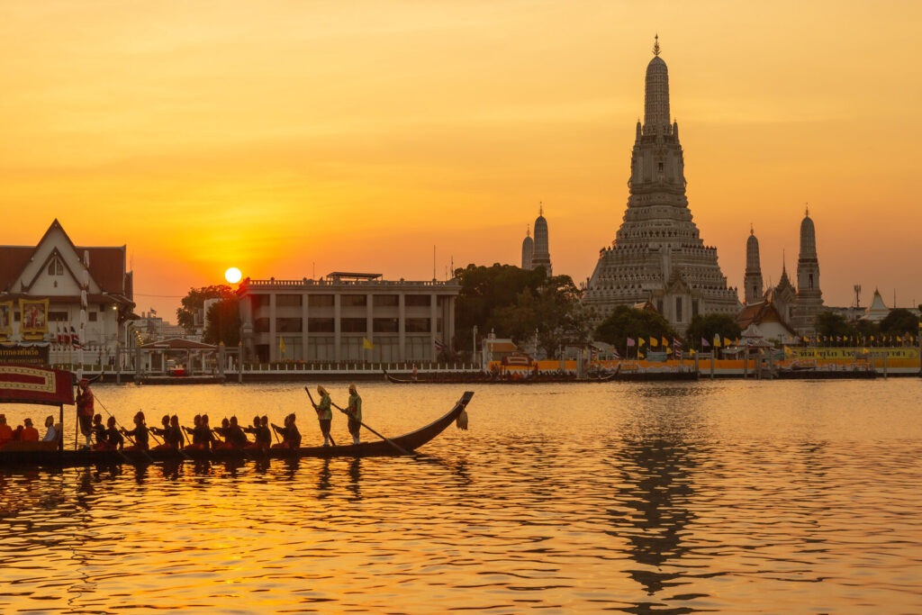 Wat Arun on the Chao Phraya river in Bangkok at sunset, with a royal barge in front