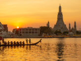 Wat Arun on the Chao Phraya river in Bangkok at sunset, with a royal barge in front
